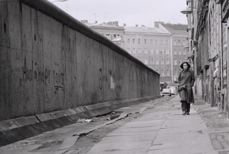 Woman walking on sidewalk next to Berlin Wall