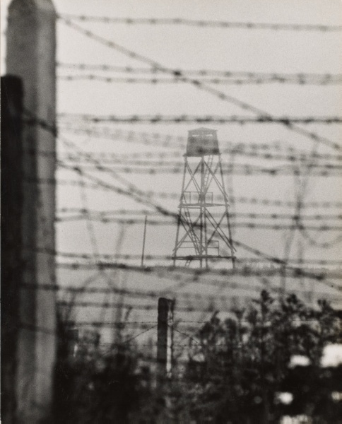 Lookout tower in the distance behind barbed wire of the Berlin Wall