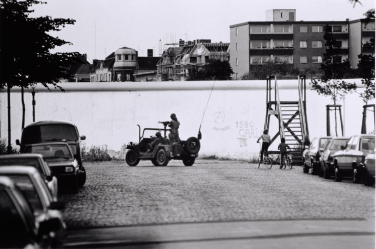 Berlin Wall patrol guards driving a military vehicle next to children biking
