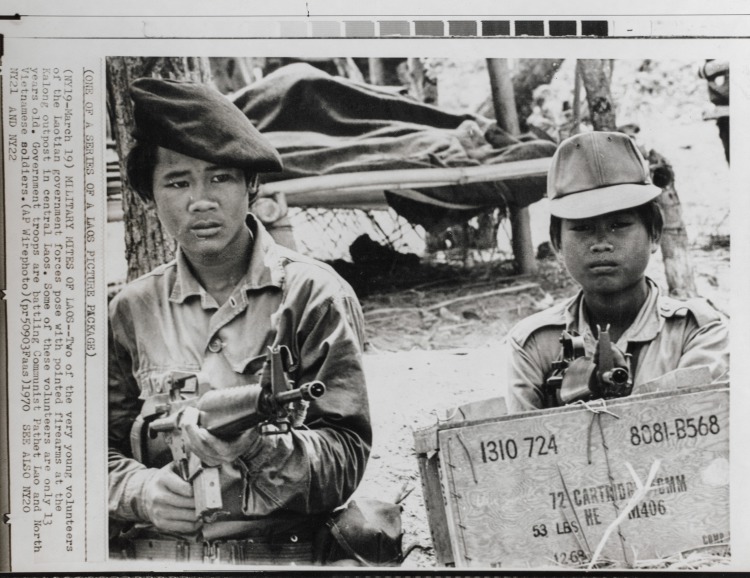 Military Mites of Laos: Two of the very young volunteers of the Laotian government forces pose with pointed firearms at the Kalong outpost in Central Laos. Some of these volunteers are only 13 years old. Government troops are battling Communist Pathet Lao and North Vietnamese soldiers