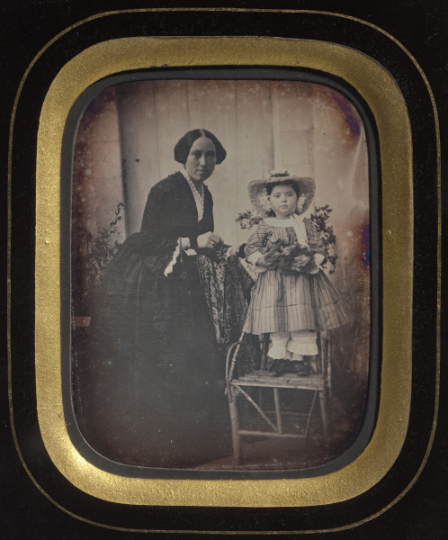 Child Standing on a Chair Holding Flowers, with Mother