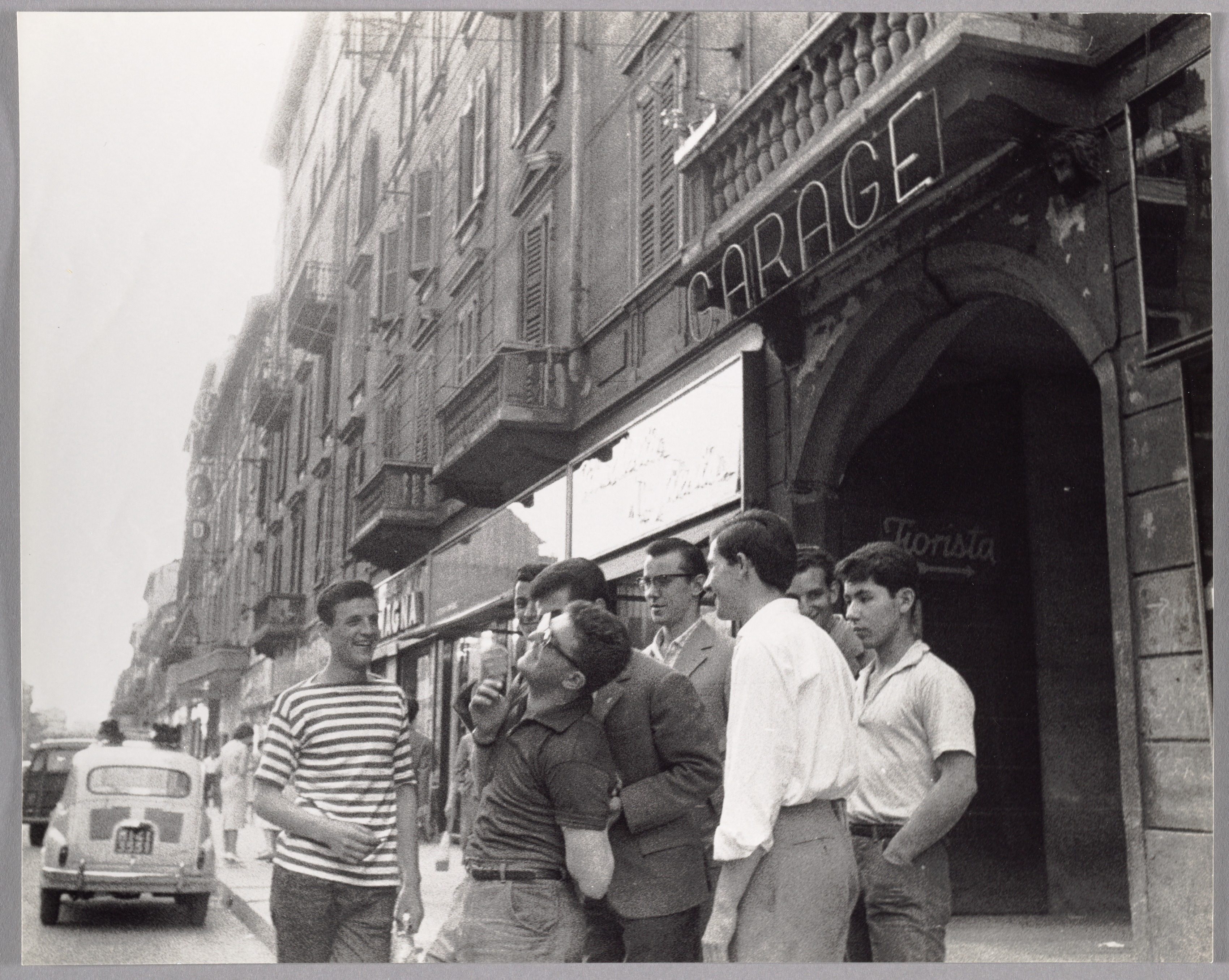 Group of Laughing Young Men on Street, in Front of Neon Garage Sign